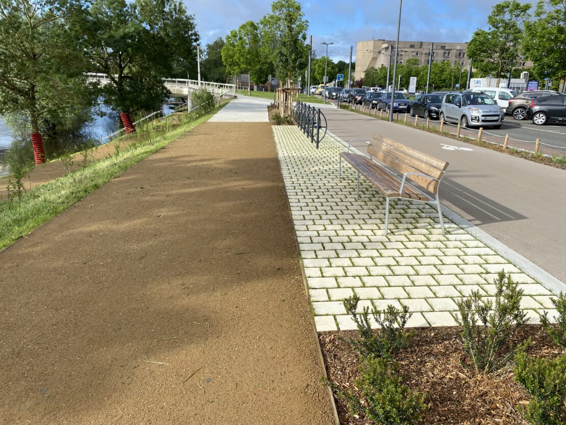 La vue principale est focus sur la route de terre et on peut voir, à droite, la nouvelle route pour vélos ainsi que les nouveaux bancs et le parterre de pierres blanches.